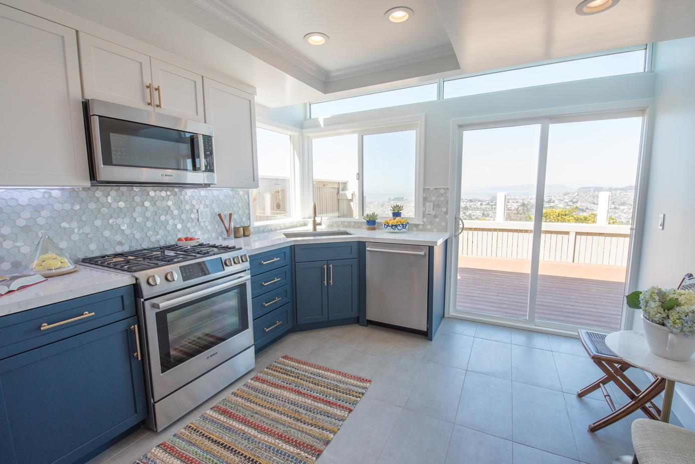 A Daly City kitchen by Kanika Design with navy-blue lower cabinets, white uppers, a hexagon tile backsplash, quartz counters, stainless appliances, and a deck with a city view.
