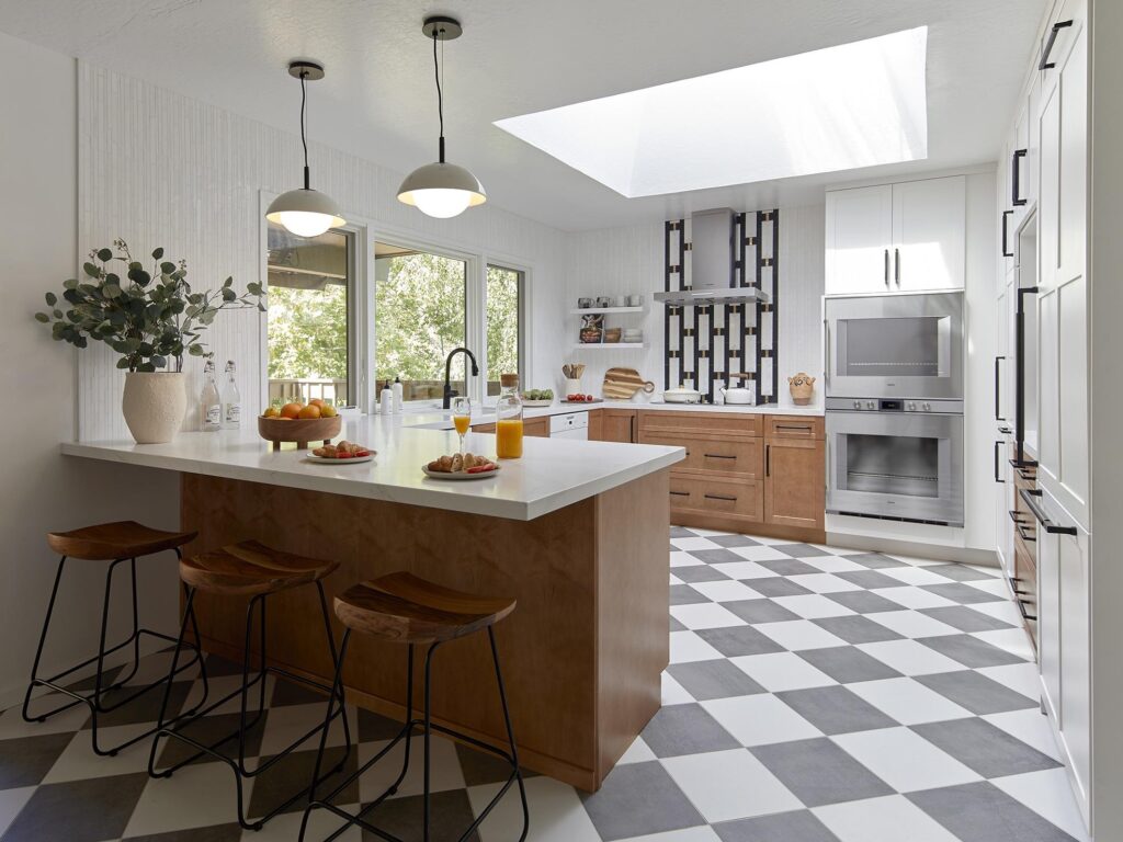A bright, modern kitchen with a wood island, black-and-white checkered floor, pendant lighting, and a skylight — designed by Kanika Design.